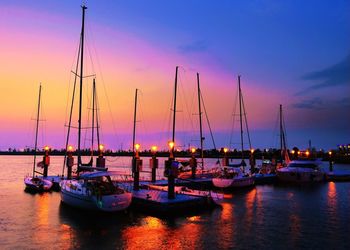 Sailboats moored at harbor against sky during sunset