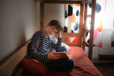 Teenager reads a book on a bed in his room, darkness, a real interior.