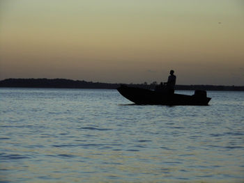 Silhouette man in boat sailing on sea against clear sky