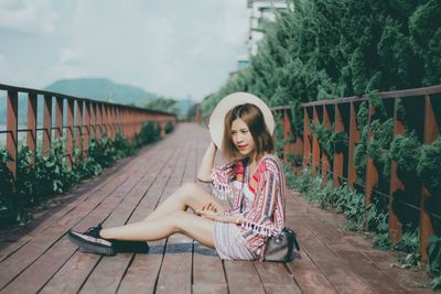 Portrait of woman sitting on railing against plants