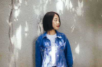 Portrait of young woman standing against wall