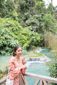 Portrait of young woman standing against waterfall