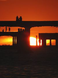 Silhouette woman standing on bridge against orange sky