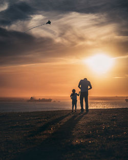 Silhouette father and daughter at beach against sky during sunset