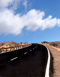 Empty road leading towards mountain against sky