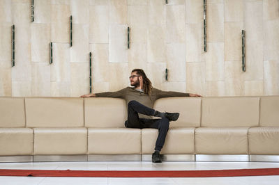 Portrait of smiling young woman sitting on sofa against wall