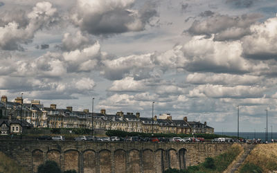 Bridge over river by buildings in city against sky