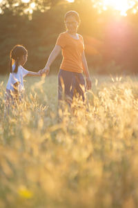 Mother with daughter standing amidst plants on field during sunset