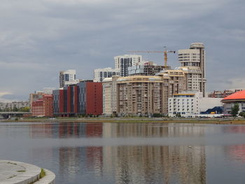 Buildings by river against sky in city