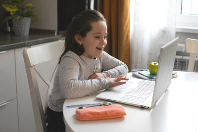 Smiling girl using laptop on table at home