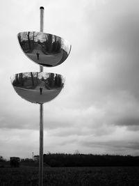 Traffic mirrors on field against cloudy sky