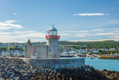 Lighthouse by sea against buildings