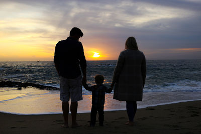 Rear view of couple standing on beach during sunset