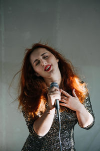 Portrait of redhead female singer woman in sparkly evening dress holding microphone on dark night