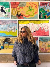 Mature woman wearing sunglasses while looking away against artistic wall