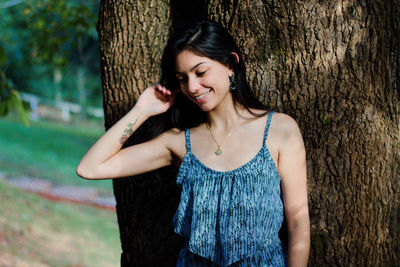 Smiling young woman standing against tree trunk