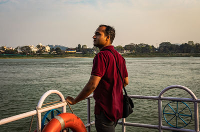 Man standing on railing by sea against sky