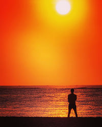 Silhouette man standing on beach against orange sky