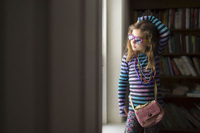 Girl wearing necklace and sunglasses standing by window at home