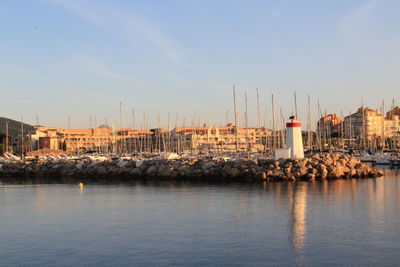 Sailboats in harbor by buildings in city against sky