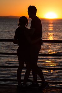 Silhouette man and woman standing on pier by sea against sky during sunset