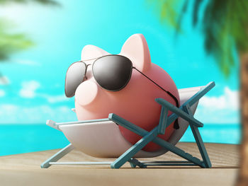 Close-up of piggy bank with sunglasses on toy deck chair