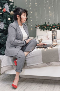 Full length of woman sitting on christmas tree