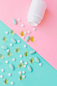 High angle view of pills spilling from bottle against blue background