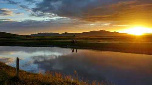 Scenic view of lake against cloudy sky during sunset