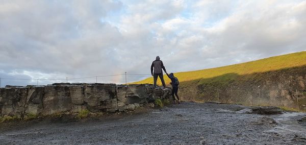 People on rock by mountain against sky