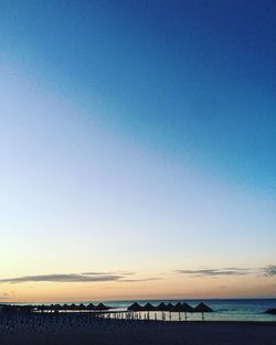 Silhouette parasols at beach against clear sky during sunset