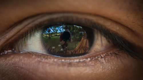 Close-up of person eye with reflection of man photographing with camera