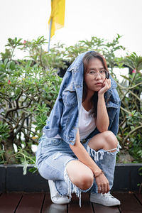 Portrait of young woman crouching against plants 