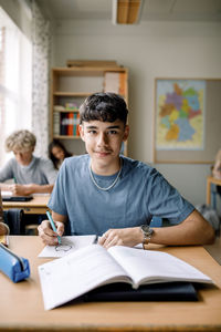 Portrait of teenage boy drawing on book in classroom