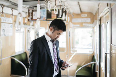 Businessman using smart phone while standing in train