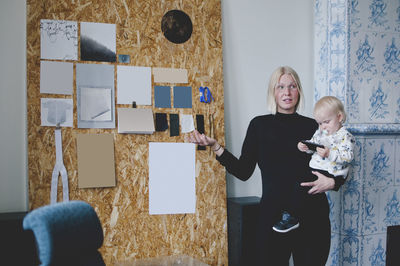 Mid adult businesswoman carrying baby girl while giving presentation in creative office