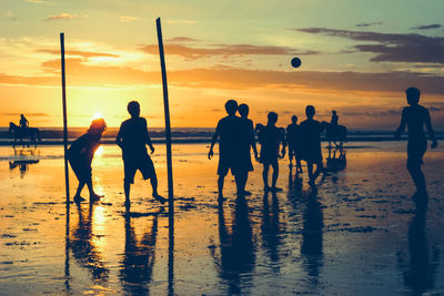 Silhouette boys playing at shore against cloudy sky during sunset