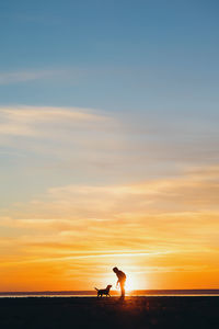 Rear view of woman standing on beach against sky during sunset