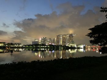 Illuminated buildings by lake against sky at night