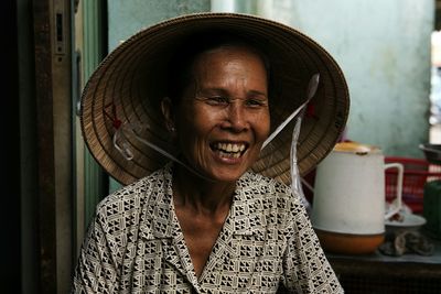 Cheerful mature woman looking away while wearing asian style conical hat at home