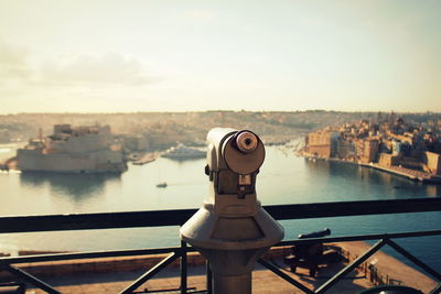 Close-up of hand-held telescope against river in city during sunset