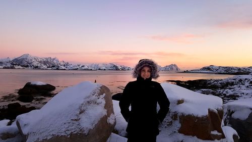 Portrait of smiling woman standing by rocks during winter at sunset