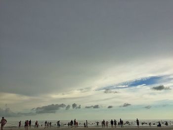 People on beach against cloudy sky