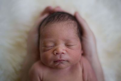 Cropped hands of parent holding newborn son on bed