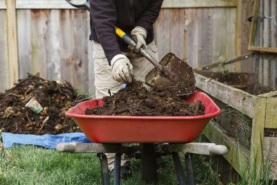 Bottom-half of person shoveling compost into red wheelbarrow in garden