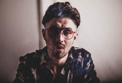 Portrait of young man with eyeglasses against wall