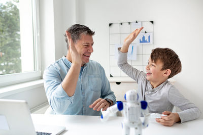 Father and son giving high-five by toy and laptop on table at home