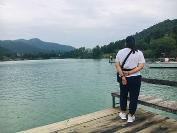 Woman standing on pier over lake against sky