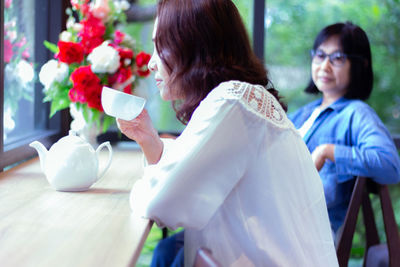 Women by flowers and coffee cup with teapot on table in cafe
