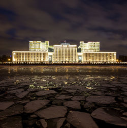 City at waterfront against cloudy sky at night